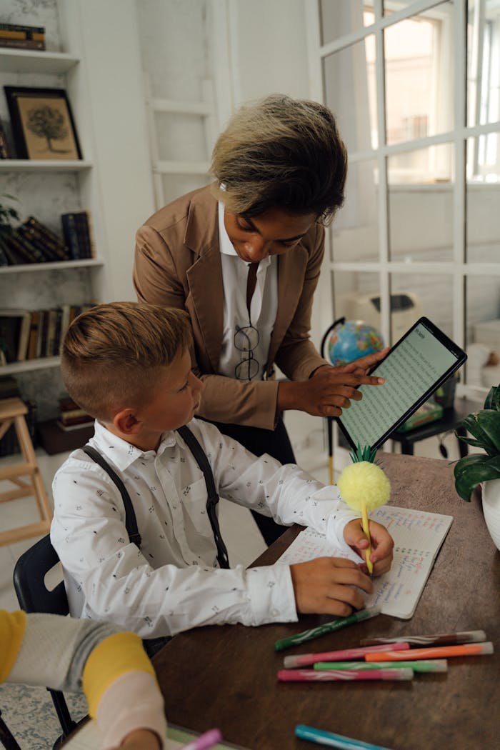 Teacher helping a student with tablet during class in a cozy, book-filled room.